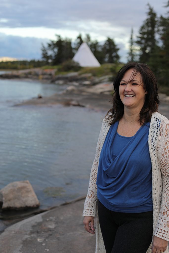 Karen MacAulay standing in front of a lake with tipi in the background